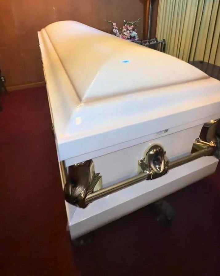 A white casket with brass handles in a quiet viewing room