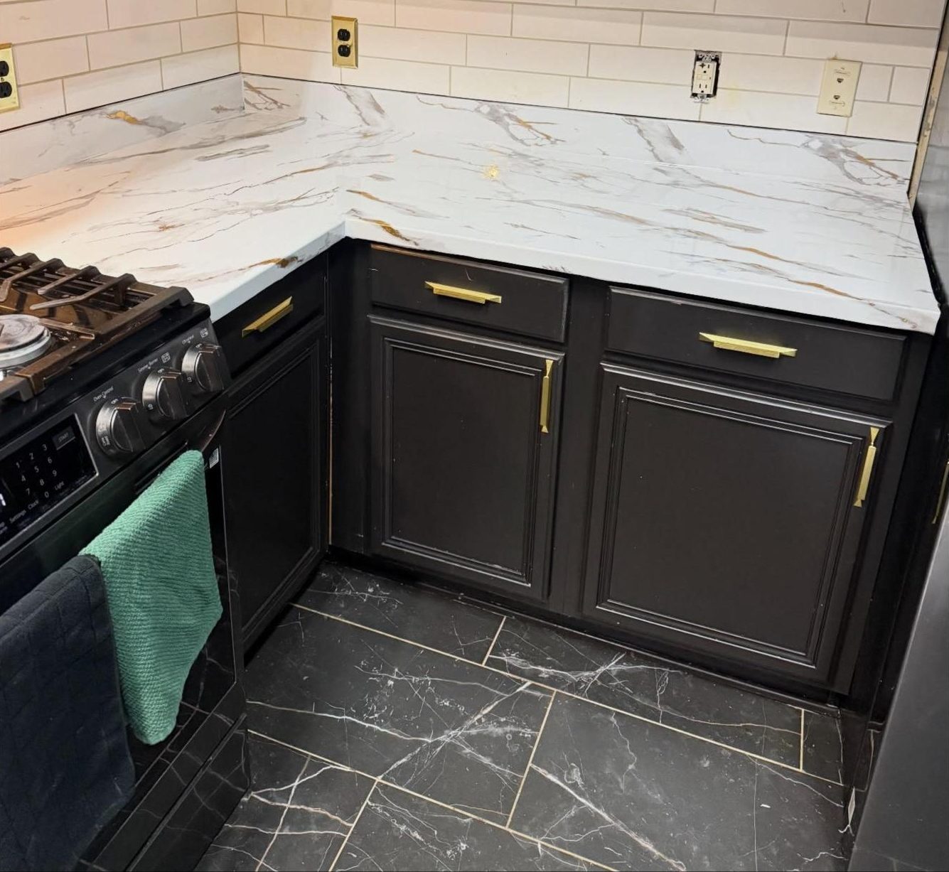 Kitchen countertop wrapped in white marble vinyl with gold veining over dark cabinets